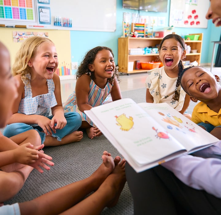 Children laughing around an adult reading a book.