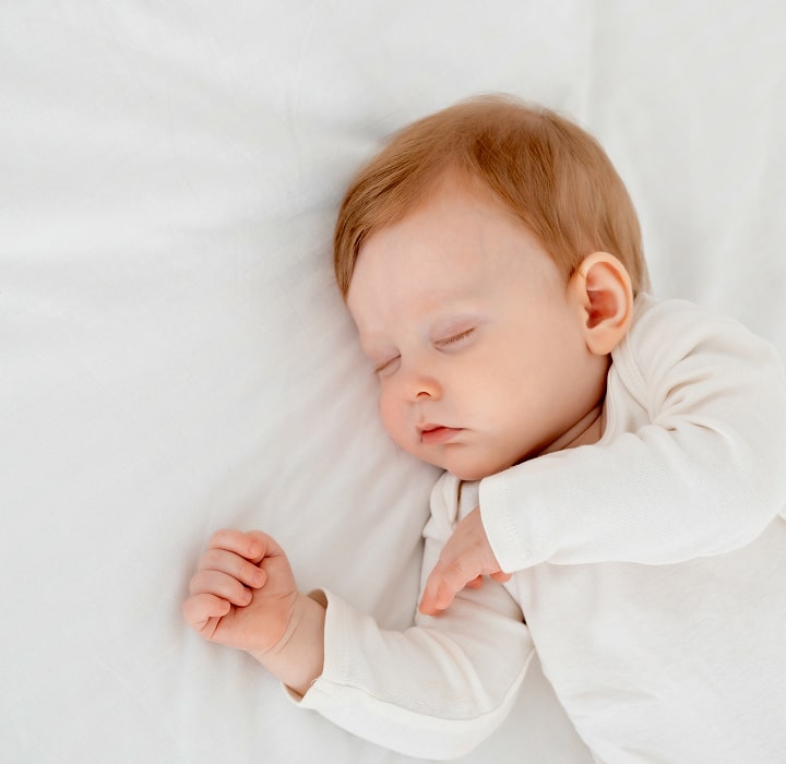 Sleeping baby in white onesie.